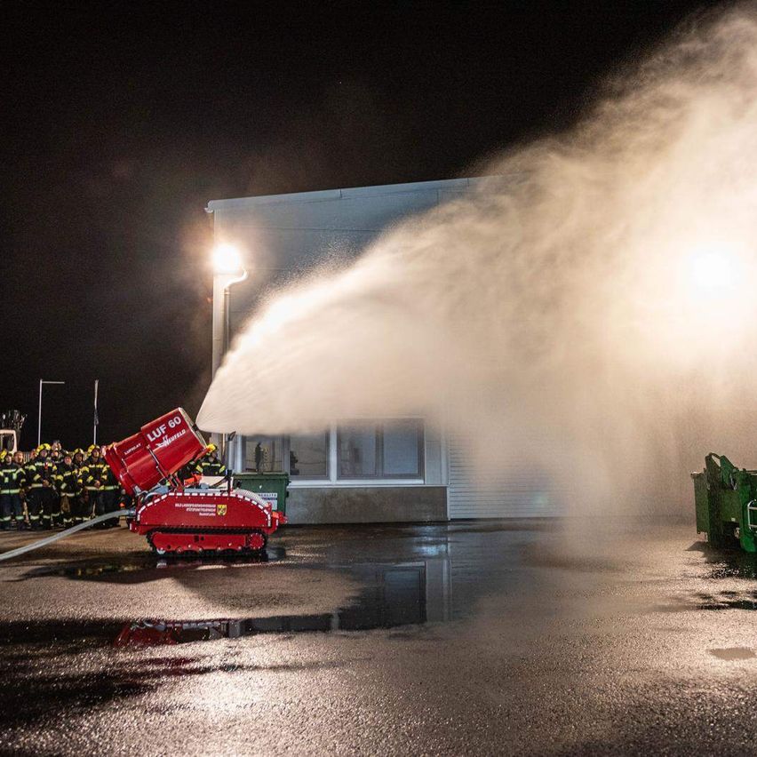 Ein Feuerwehrwagen sprüht Wasser in einem Parkplatz bei Nacht in die Luft. Der Feuerwehrwagen ist rot.