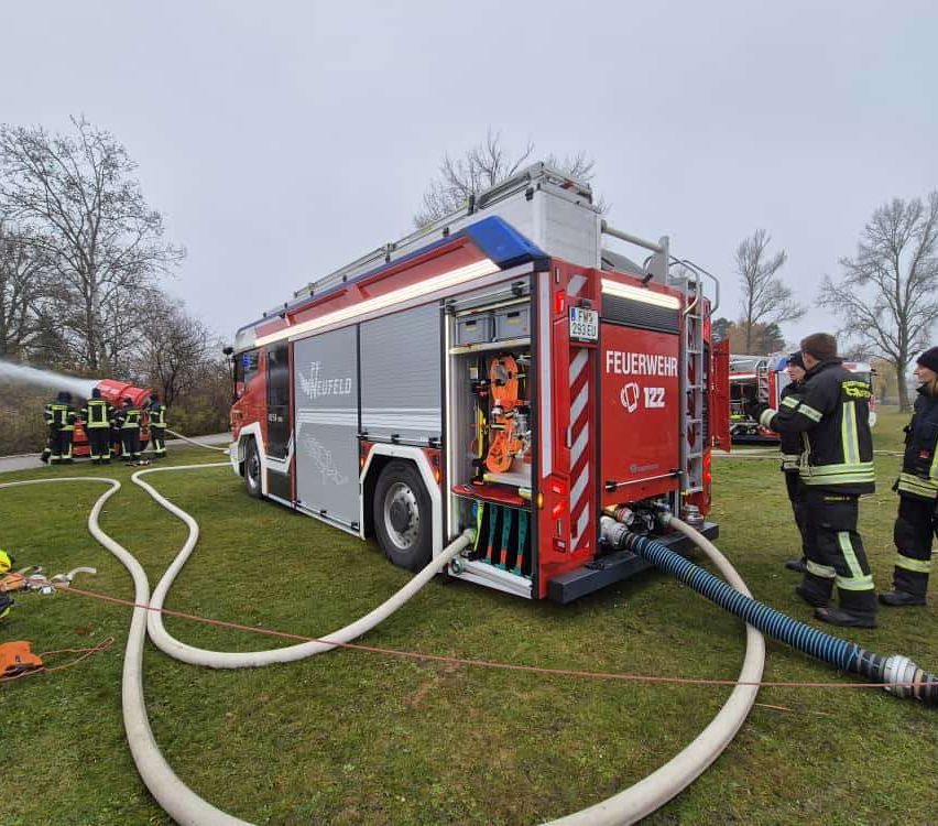 Ein roter Feuerwehrwagen mit der Nummer 122 steht auf einem Rasenfeld. Ein Feuerwehrmann steht neben dem Fahrzeug.