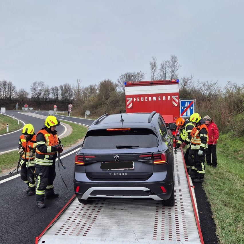 Feuerwehrleute bereiten sich darauf vor, einen dunkelgrauen Volkswagen SUV abzuschleppen. Die Feuerwehrleute tragen Helme und Handschuhe. Ein Feuerwehrwagen ist hinter dem SUV geparkt.