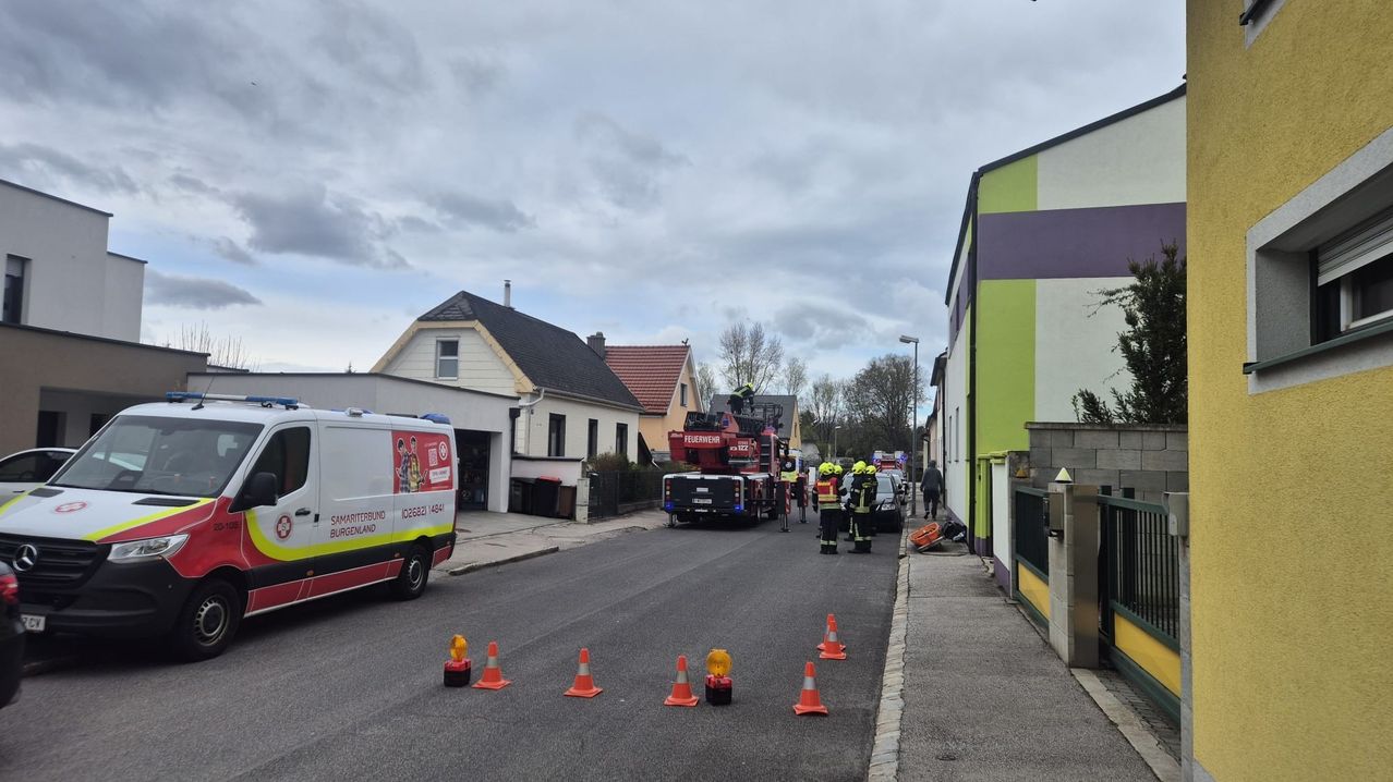 Ein Feuerwehrauto mit Feuerwehrleuten steht auf der Straße. Verkehrskegel markieren das Gebiet. Ein weißer Lieferwagen ist am Straßenrand geparkt.