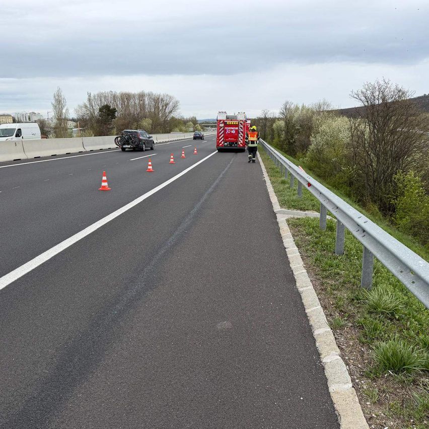 Eine Autobahn mit einem Feuerwehrwagen am Straßenrand, Verkehrskegel, die einen Bereich markieren, und einer Person in Schutzausrüstung.