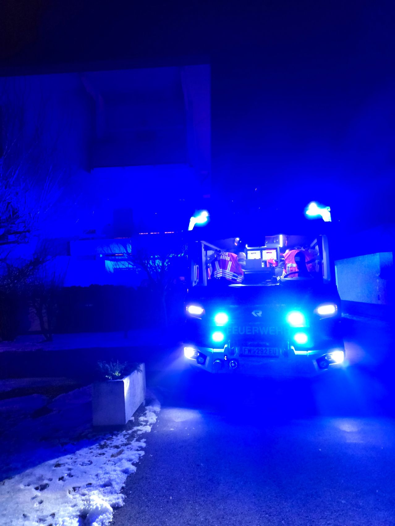 Ein Feuerwehrauto mit eingeschalteten Lichtern steht nachts auf der Straße.