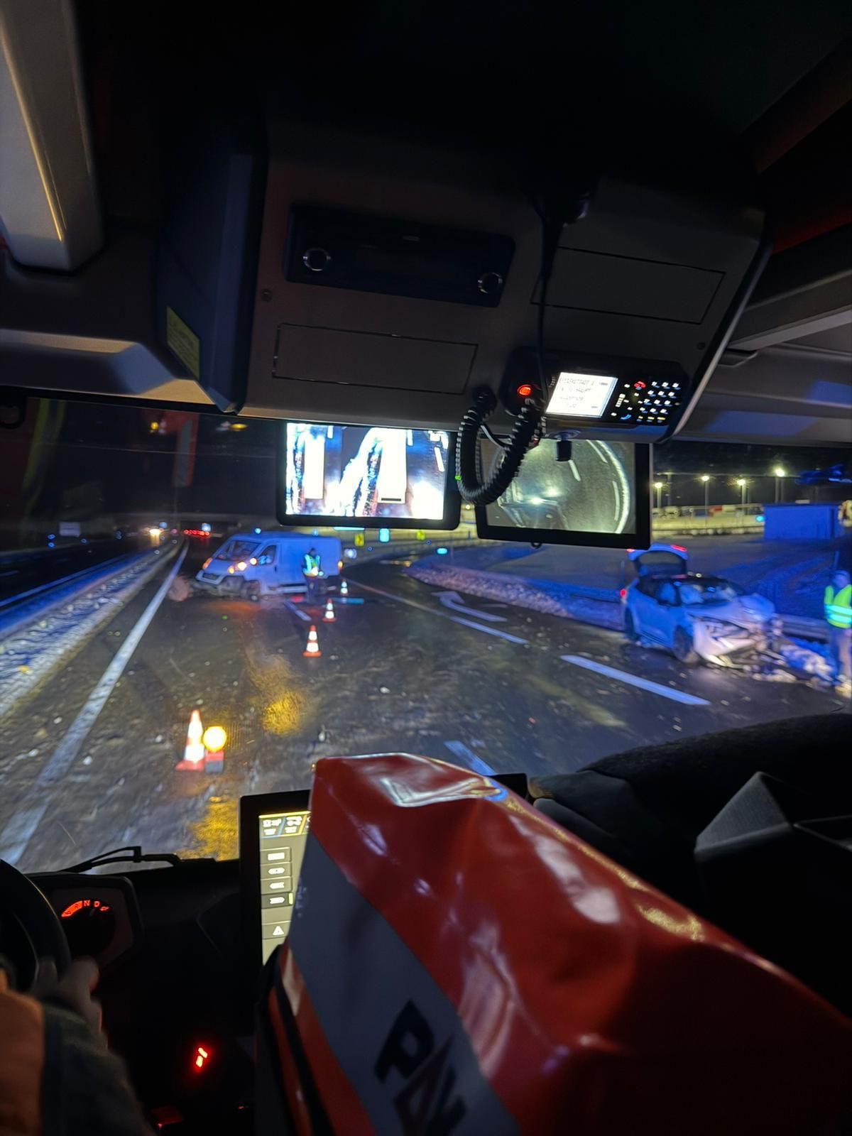 Ein Blick aus dem Inneren eines Busses zeigt ein beschädigtes Auto am Straßenrand mit Kegel und einer Person in einer Warnweste.