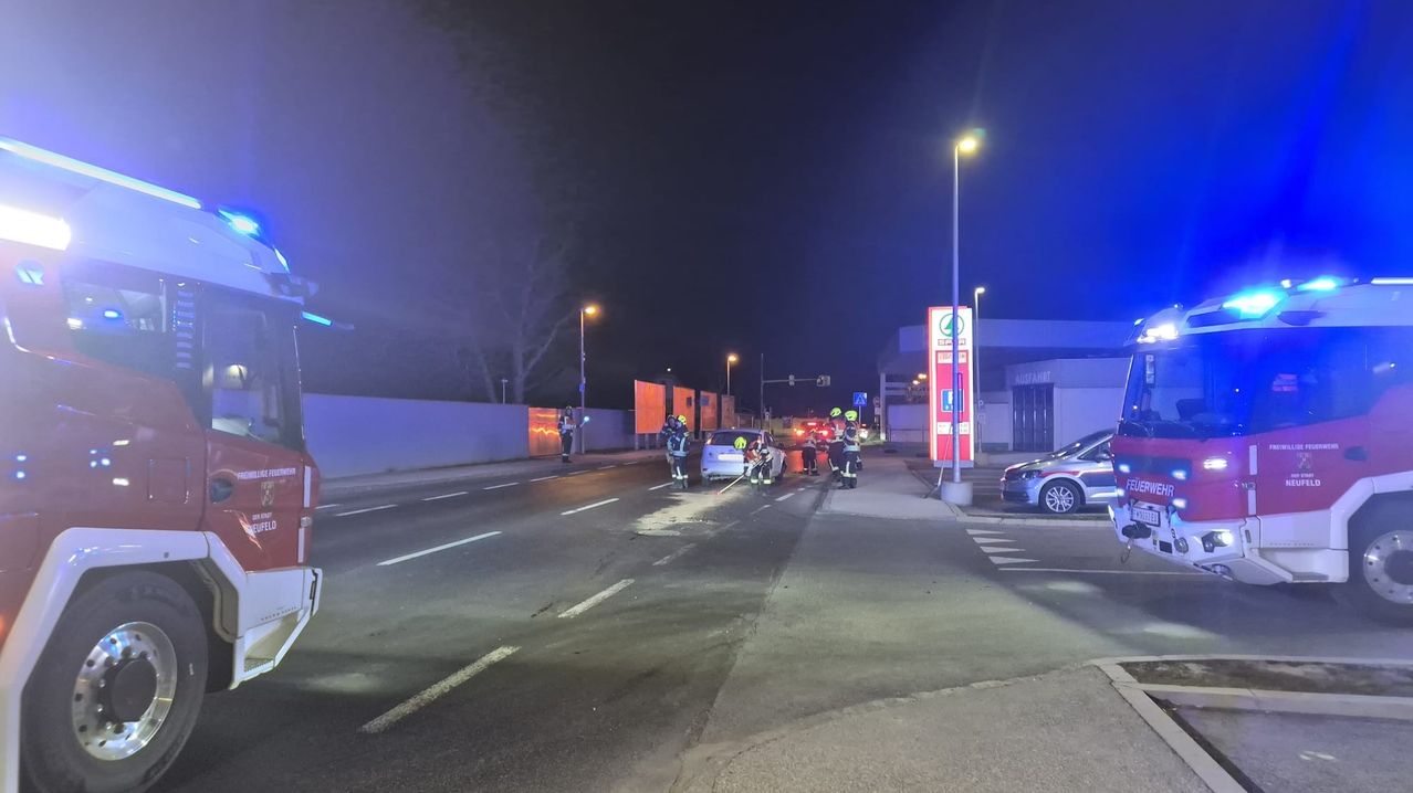 Rettungskräfte sind an der Unfallstelle im Dunkeln, mit blinkenden Lichtern, die das Gebiet beleuchten. Zwei Autos sind beteiligt, und Arbeiter räumen Trümmer weg.