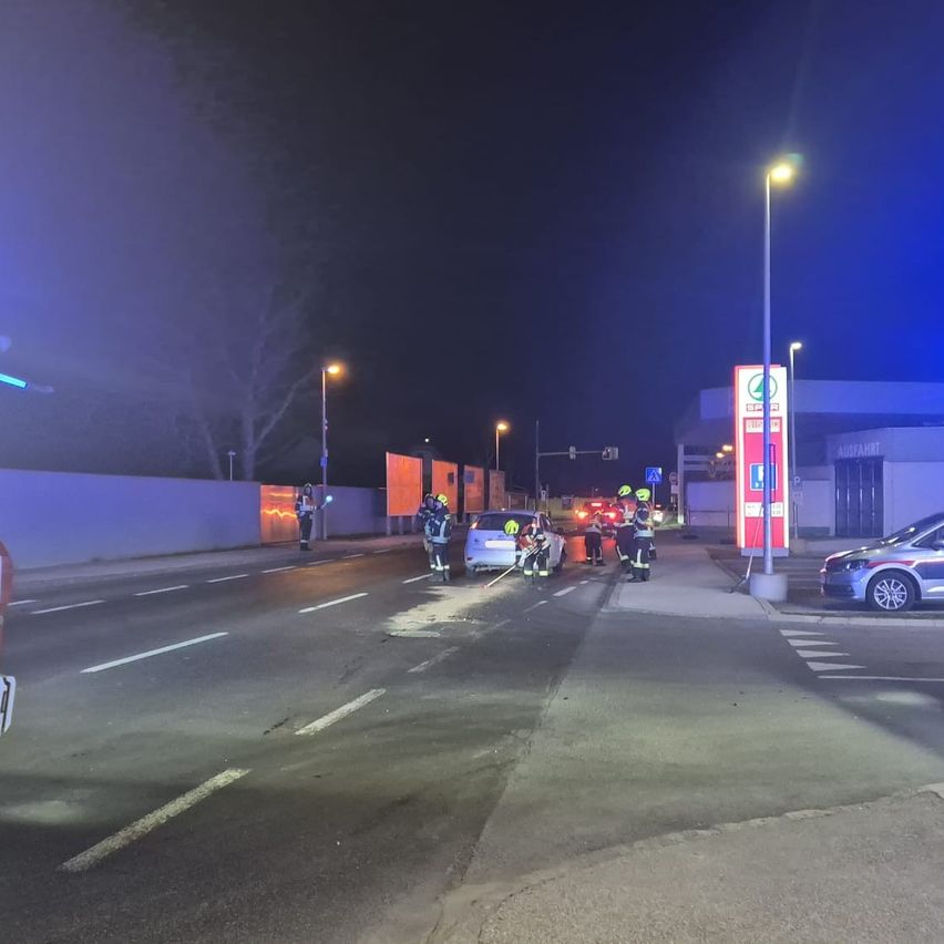 Rettungskräfte sind an der Unfallstelle im Dunkeln, mit blinkenden Lichtern, die das Gebiet beleuchten. Zwei Autos sind beteiligt, und Arbeiter räumen Trümmer weg.