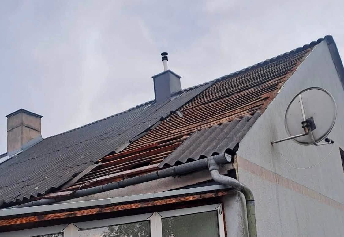 Ein Haus mit einem beschädigten Dach und einem Schornstein darauf. Das Dach besteht aus Metallblechen und hat einen Dachrinnen an der Seite. Das Haus hat ein Glasfenster und eine Tür.