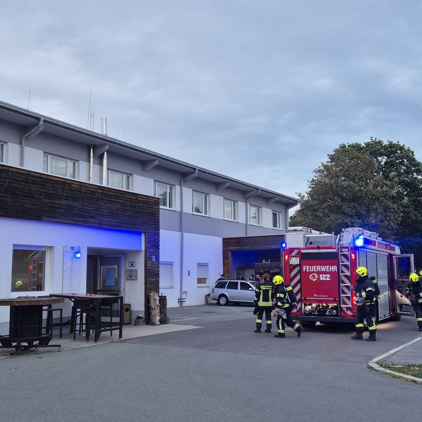 Feuerwehrleute reagieren auf einen Notfall in einem Gebäude mit einem Restaurant davor. Sie gehen auf einen Feuerwehrwagen mit eingeschalteten Lichtern zu.