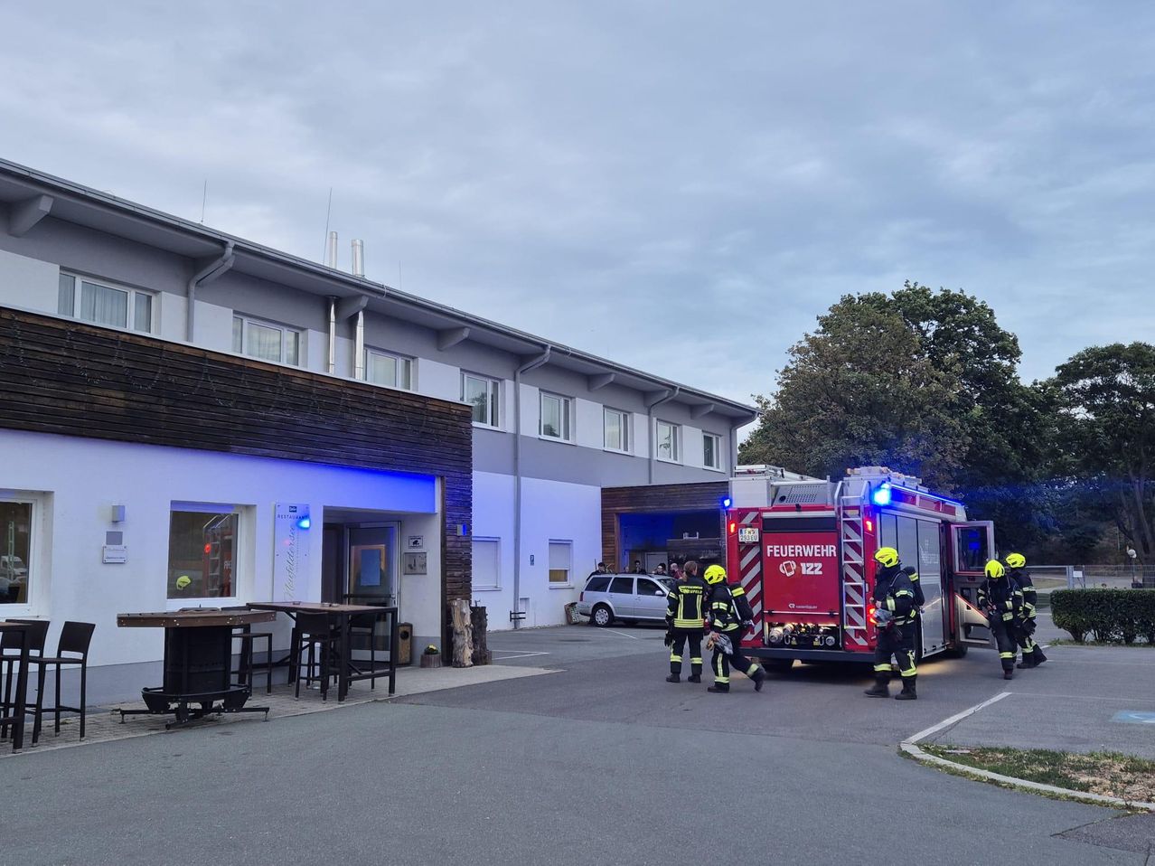 Feuerwehrleute reagieren auf einen Notfall in einem Gebäude mit einem Restaurant davor. Sie gehen auf einen Feuerwehrwagen mit eingeschalteten Lichtern zu.