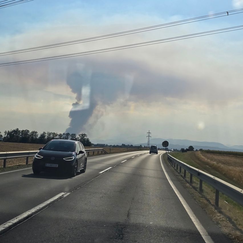 Ein Auto fährt auf einer Autobahn, wobei in der Ferne eine große Rauchsäule aufsteigt.