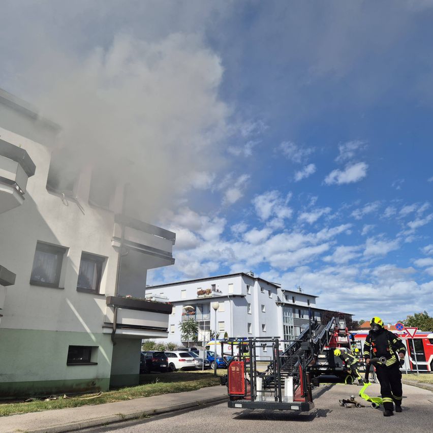 Feuerwehrleute reagieren auf einen Brand in einem Mehrfamilienhaus, aus dessen Fenstern Rauch aufsteigt.