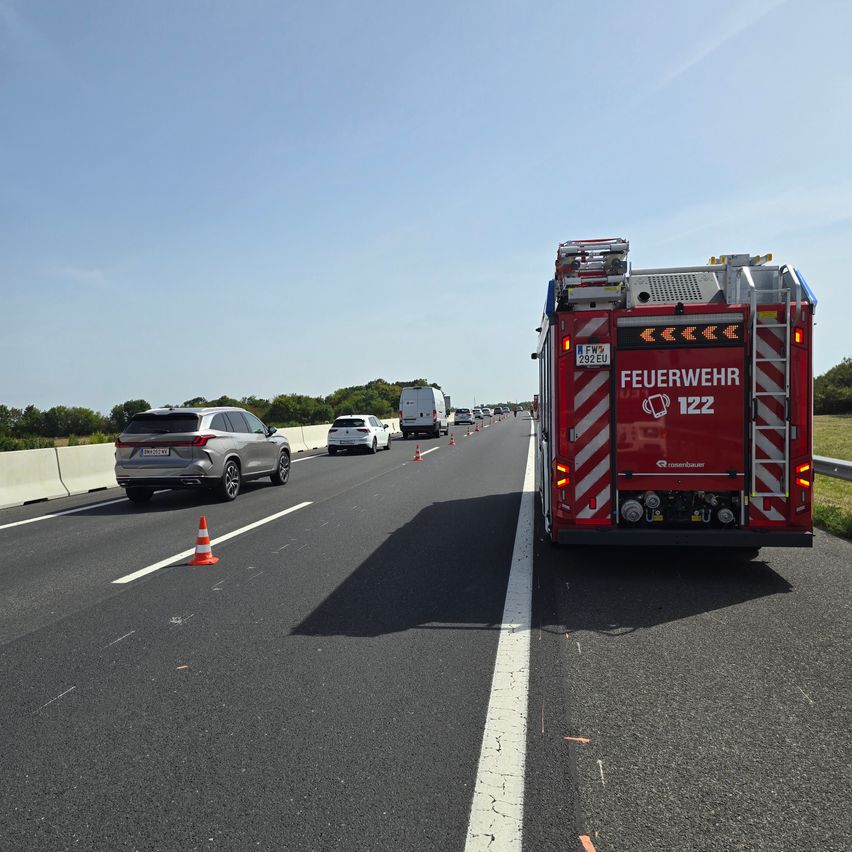 Ein Feuerwehrauto ist am Straßenrand eines Highways geparkt, mit Verkehrskegel und Fahrzeugen dahinter.
