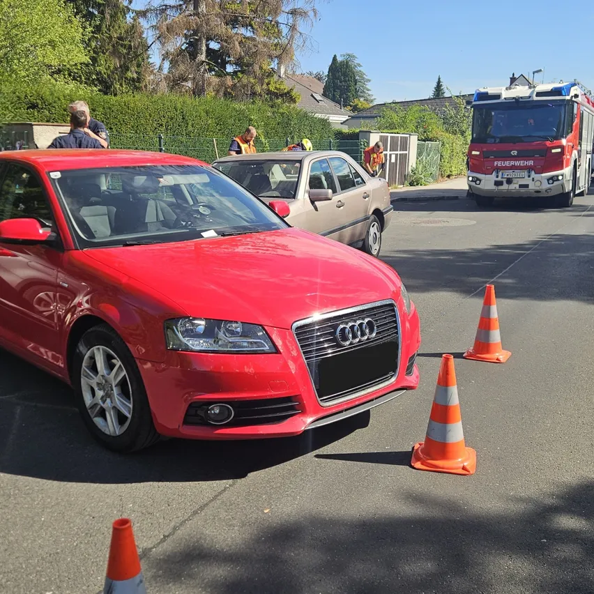 Ein roter Audi-Wagen ist auf der Straße geparkt, mit Verkehrskegel drum herum. Ein Feuerwehrwagen ist in der Nähe geparkt, und mehrere Leute stehen herum.