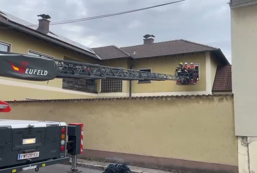 Ein Feuerwehrauto mit dem Wort Eufeld steht vor einem Haus, dessen Fenster mit einer Leiter versehen ist.
