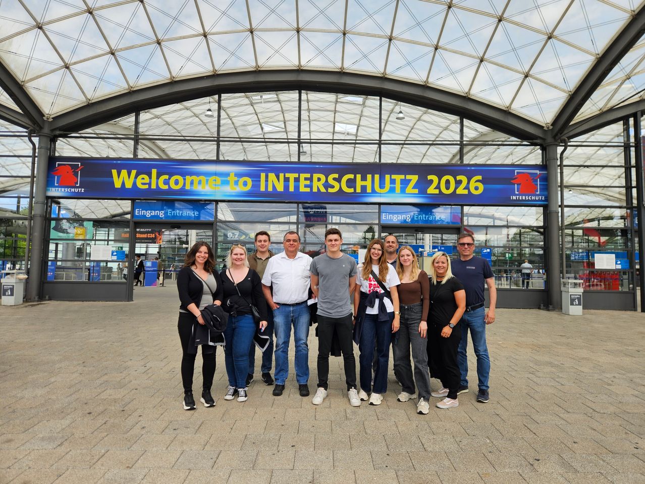 Eine Gruppe von Menschen steht vor einem großen Gebäude mit dem Schild Willkommen bei INTERSCHUTZ 2026.