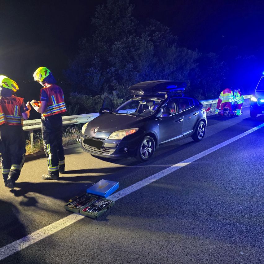 Rettungskräfte helfen einer verletzten Person bei einem nächtlichen Verkehrsunfall, einem beschädigten Auto und einer Werkzeugkiste auf der Straße.