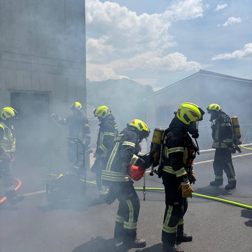 Eine Gruppe von Feuerwehrleuten in gelben Helmen übt ihre Fähigkeiten mit Rauch und Ausrüstung in einem Trainingsbereich.
