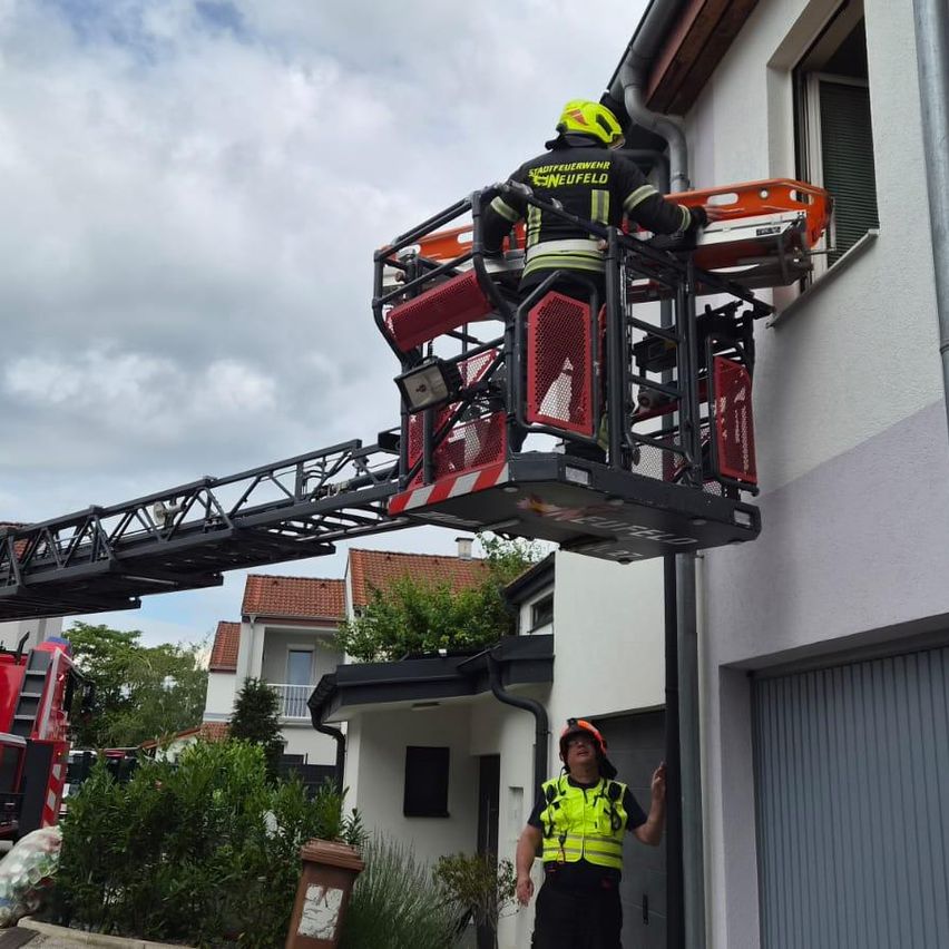 Ein Feuerwehrmann ist auf einer Leiter und erreicht ein Fenster eines Hauses. Ein weiterer Feuerwehrmann steht unten und beobachtet.