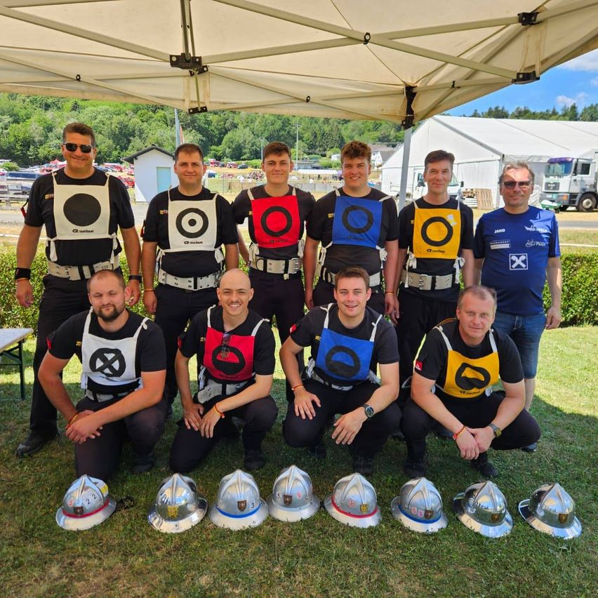 Eine Gruppe von Männern in Sicherheitswesten posiert für ein Foto mit Helmen vor ihnen unter einem Zelt.