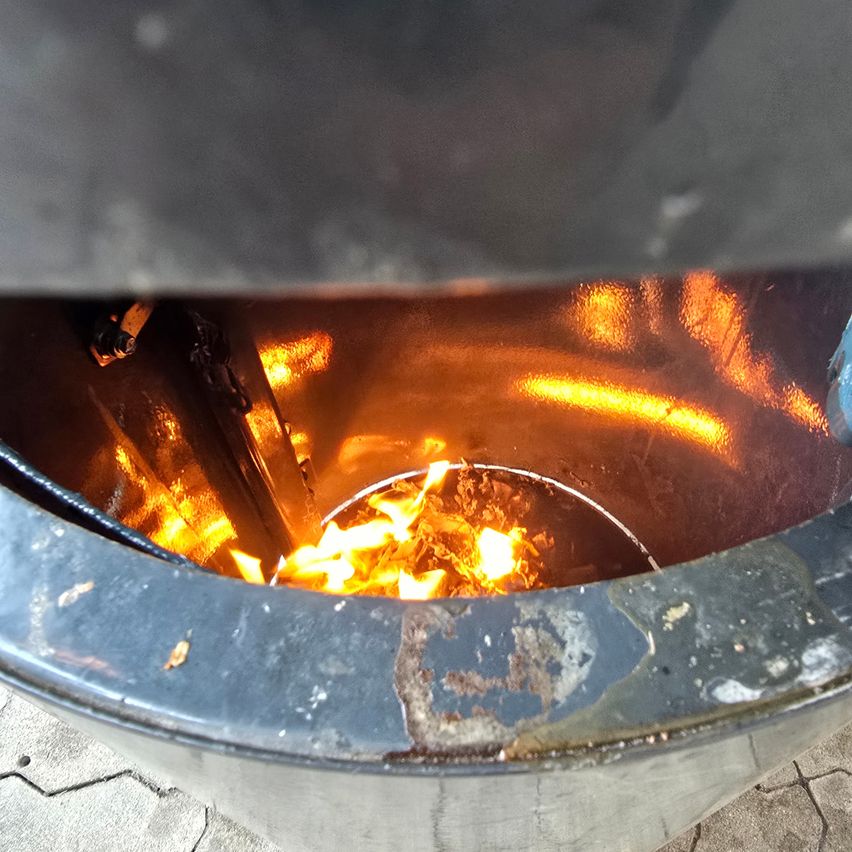 Eine Nahaufnahme eines Metallbehälters mit einem brennenden Feuer im Inneren, das warmes Licht und Schatten auf das Innere des Behälters wirft.