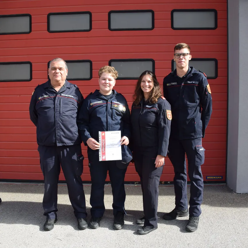 Vier Feuerwehrleute stehen vor einer roten Feuerwehrstationentür.