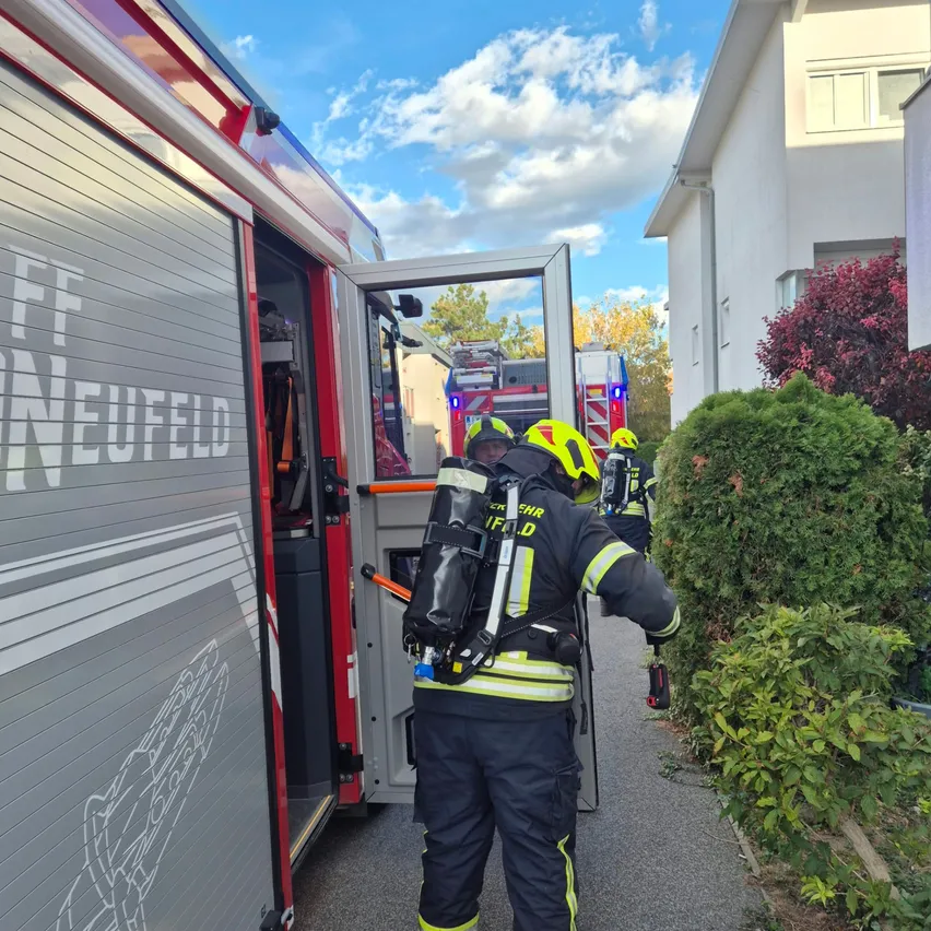 Ein Feuerwehrmann in voller Ausrüstung, einschließlich eines gelben Helms, verlässt einen Feuerwehrwagen mit dem Wort 'Neuenfeld' an der Seite.