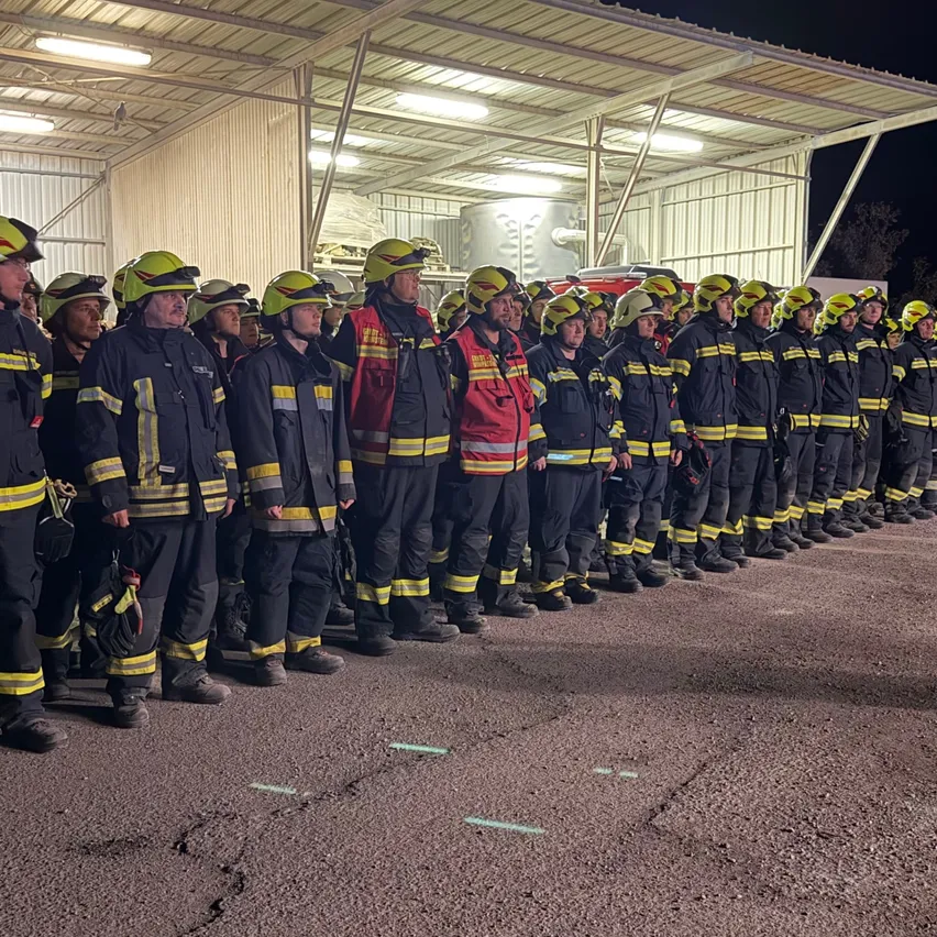 Eine Gruppe von Feuerwehrleuten in voller Ausrüstung steht nachts vor einer Feuerwache in einer Reihe.
