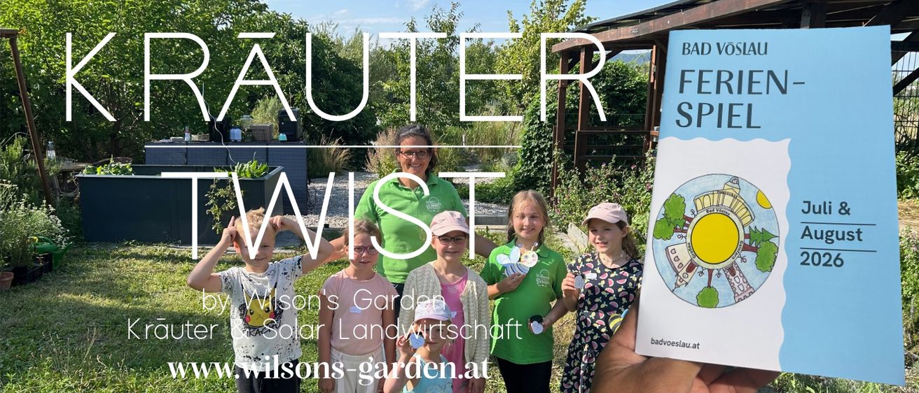 Eine Gruppe von Kindern und einer erwachsenen Frau in grünen Shirts posiert für ein Foto im Garten, wobei der Text 'Wilson's Garden & Solar Landwirtschaft' sichtbar ist.