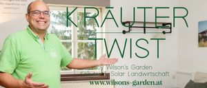 Ein Mann in einem grünen T-Shirt steht vor einem Fenster mit Blick auf Bäume und präsentiert ein Konzept namens Kraut Twist von Wilson's Garden.