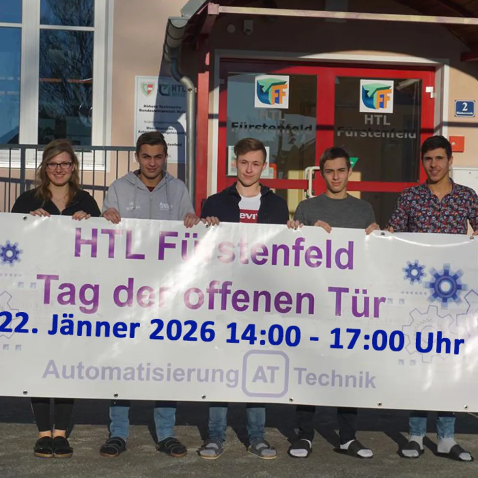 Fünf Personen stehen vor einem Gebäude und halten ein Banner. Das Banner trägt den Text 'HTL Furstenfeld Tag der offenen Tür 22. Jänner 2026 14:00-17:00 Uhr Automatisierung AT Technik'.