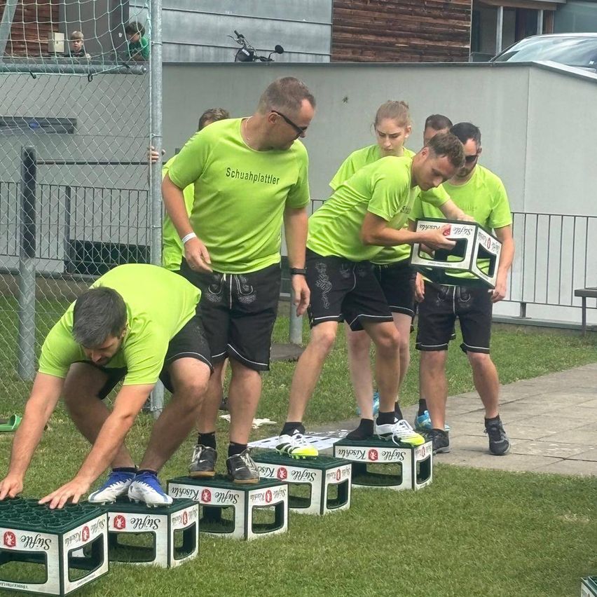 Eine Gruppe von Menschen in grünen Shirts und Shorts nimmt an einer Schuhstapel-Veranstaltung auf einem Rasenfeld teil.