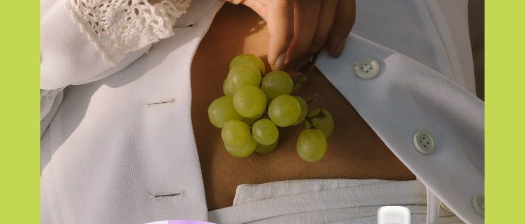 Eine Frau hält eine Traube grüner Trauben auf ihrem Bauch. Der Text lautet 'Frucht der Götter' für Kraft und lange Gesundheit.