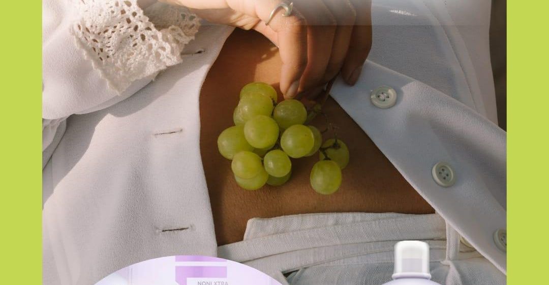 Eine Frau hält eine Traube grüner Trauben auf ihrem Bauch. Der Text lautet 'Frucht der Götter' für Kraft und lange Gesundheit.