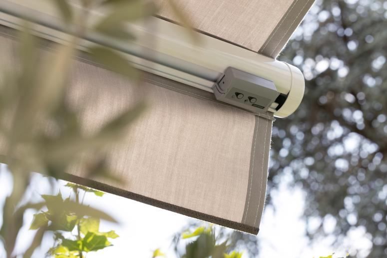 Nahaufnahme eines Vordachs mit einem versenkbaren Sonnenschutz, unter einem Baum positioniert, mit einem sichtbaren Kontrollschalter.