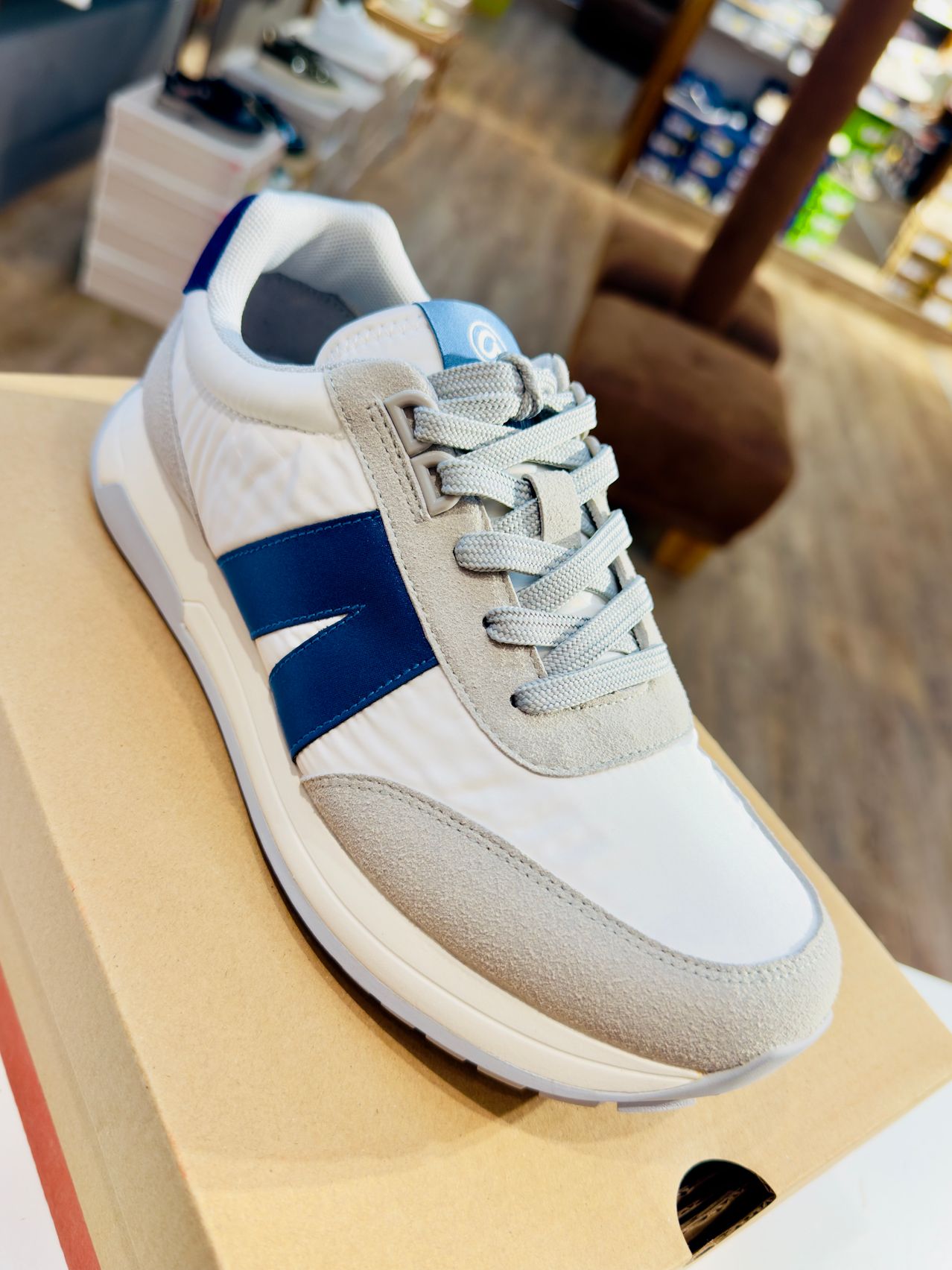 Ein weißer und blauer Sneaker mit grauer Sohle liegt in einem Geschäft auf einem Karton.