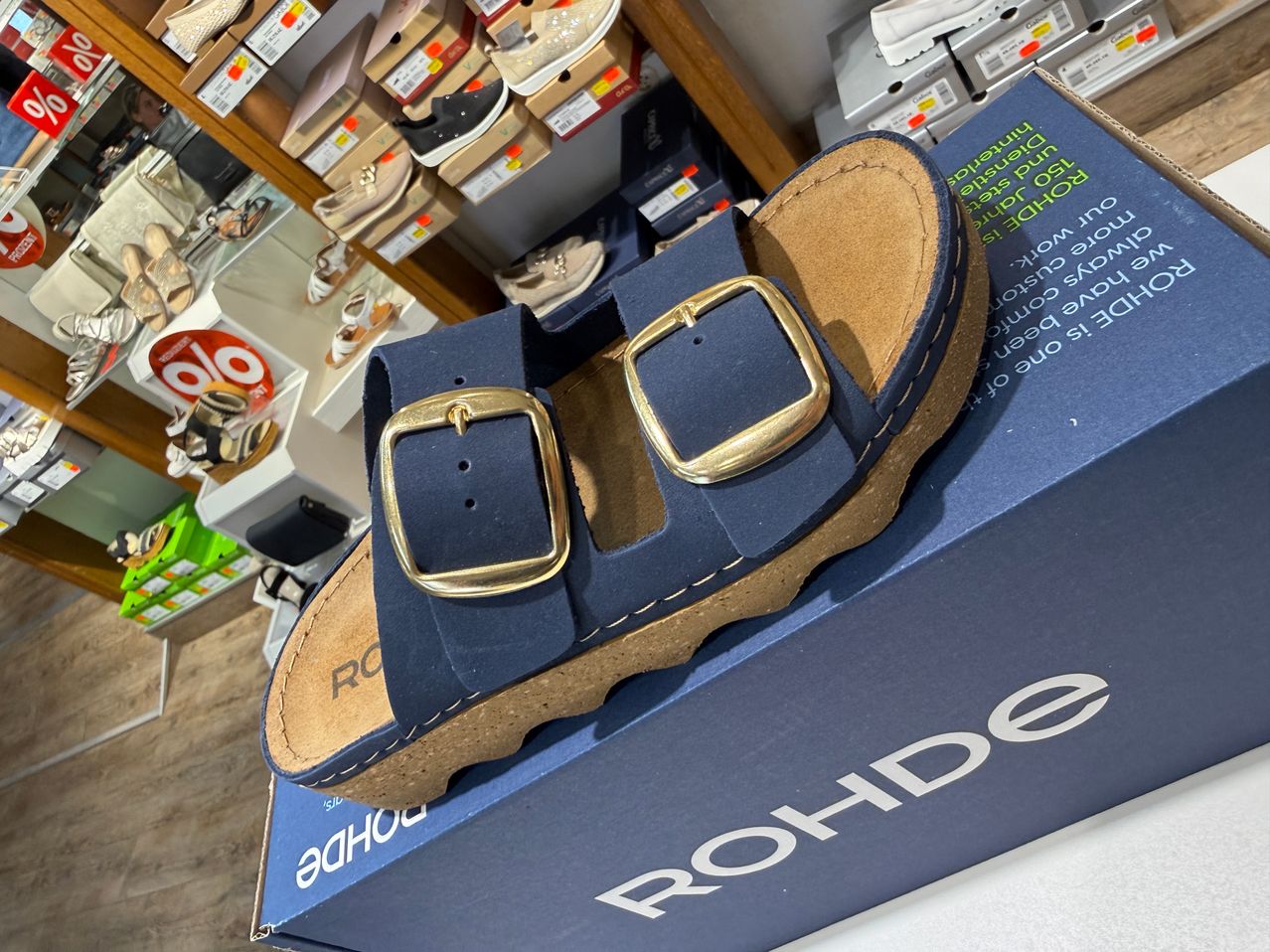 A pair of navy blue sandals with gold buckles on a blue box labeled Rohde.