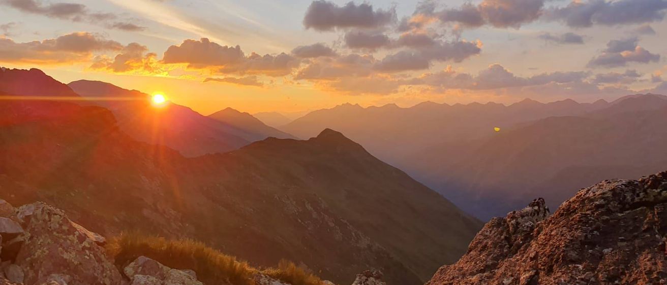 Sonnenuntergang über einer rauen Bergkette mit klarem Himmel und verstreuten Wolken.
