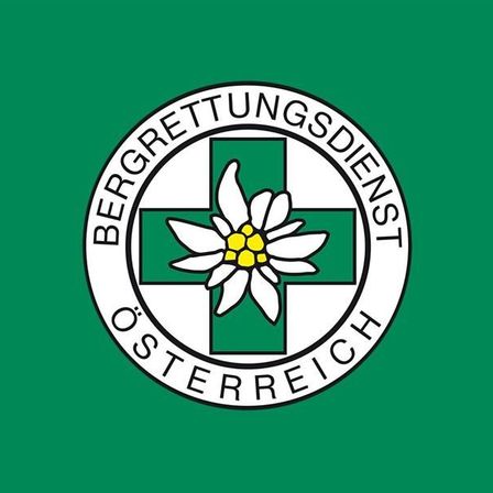 Das Emblem des Österreichischen Bergrettungsdienstes mit einer weißen Blume und einem grünen Kreuz in der Mitte auf grünem Hintergrund.