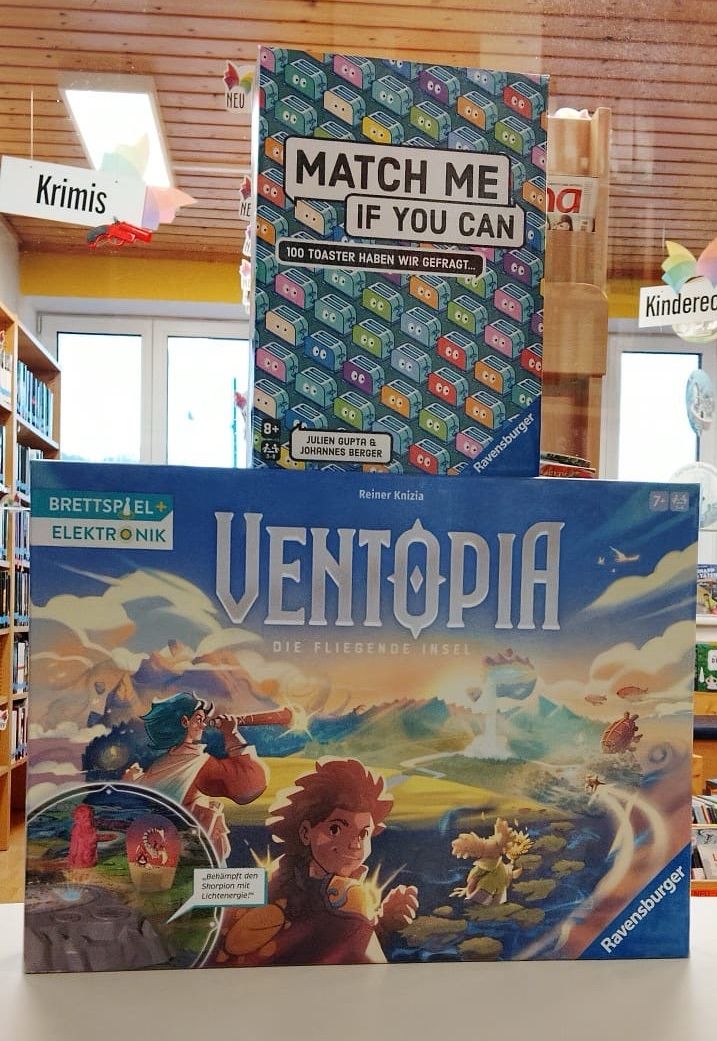 Das Brettspiel Ventopia, Die Fliegende Insel, ist in einem Geschäft ausgestellt. Ein Karton Match Me, wenn du kannst, ist darüber platziert.