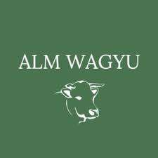 Grüner Hintergrund mit weißem Text 'ALM WAGYU' über einer weißen Illustration des Kopfes einer Kuh.