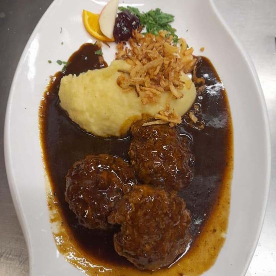 Ein Teller mit Fleischbällchen in brauner Soße mit Kartoffelpüree, Cranberry-Sauce und gebratenen Zwiebeln.