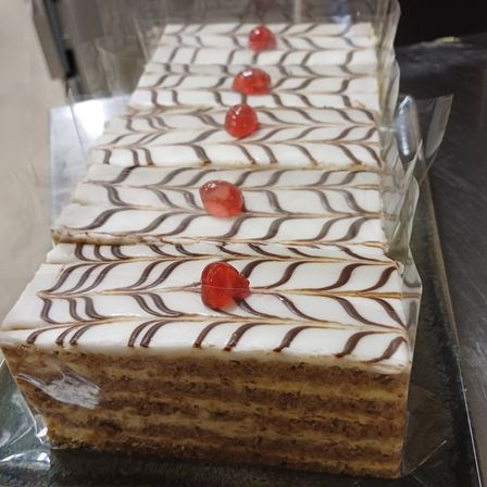 Ein Stapel von mehrschichtigen Kuchen, die mit weißer Glasur und schokoladenfarbenen Wirbeln überzogen sind und mit roten Kirschbonbons gekrönt sind. Jeder Kuchen ist einzeln in Klarsichtfolie eingewickelt.