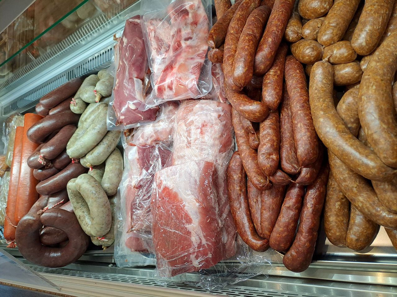 Eine Fleischtheke mit verschiedenen Fleischsorten. Würste und eingewickelte Fleischstücke sind ordentlich angeordnet. Die Würste haben verschiedene Farben und Formen.