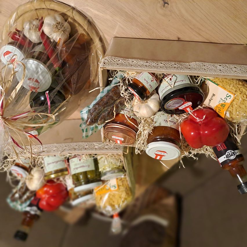 Zwei Schachteln mit verschiedenen Gewürzen und Saucen sind auf einem Holztisch angeordnet, einschließlich Gläser mit Saucen, Gewürzgurken und einer Flasche Chilisauce.