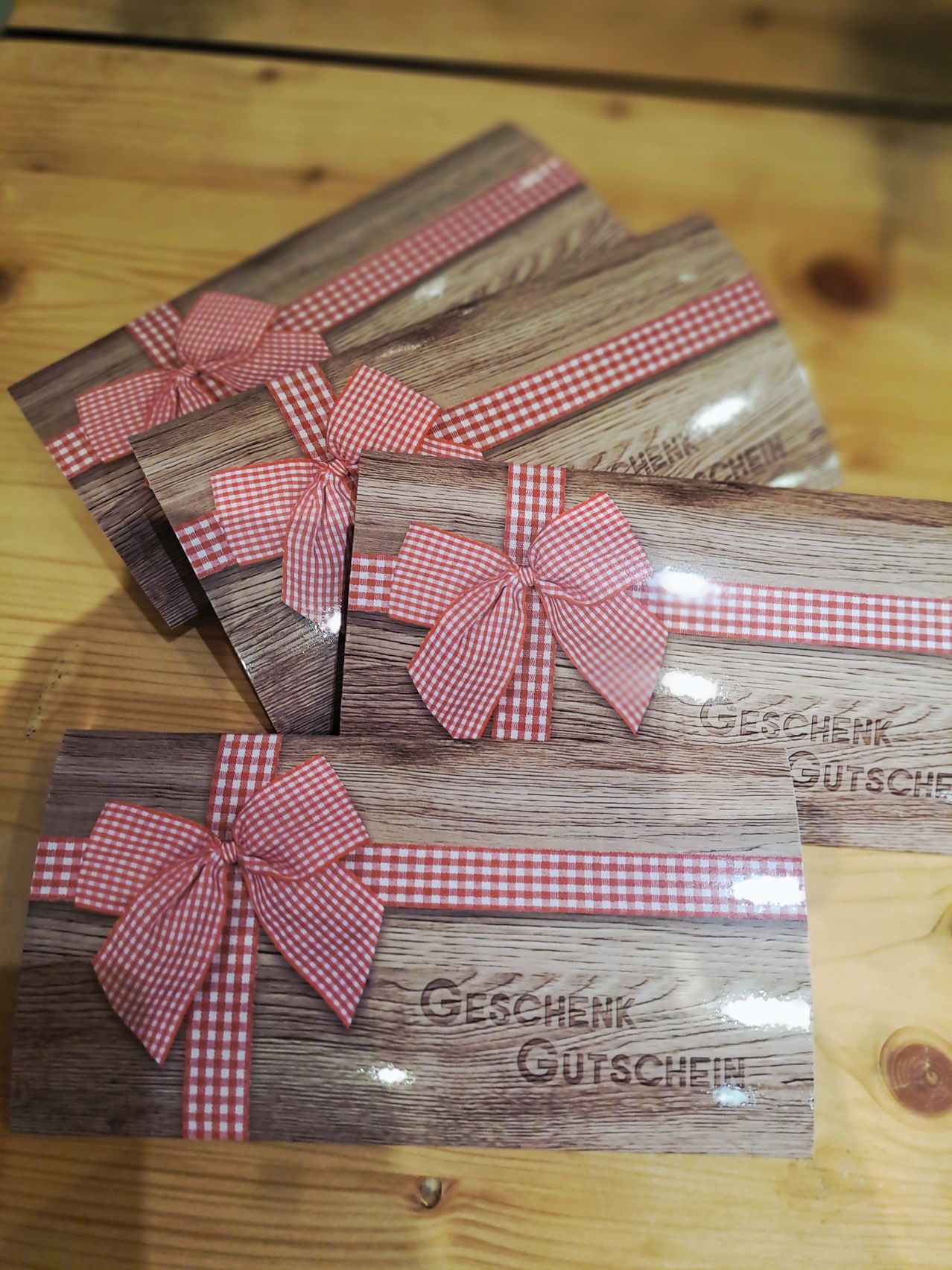Ein Stapel rustikaler Geschenkgutscheine aus Holz mit roten Gingham-Schleifen auf einer Holzoberfläche. Die Karten sind mit Geschenk Gutschein beschriftet.
