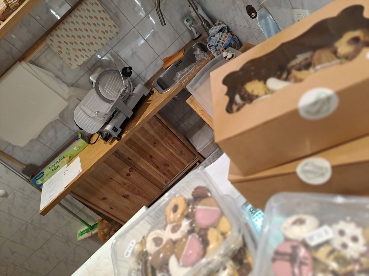 Eine Küchentheke mit einem Schneidegerät, zwei Schachteln mit verschiedenen Keksen und einer Spüle. Die Küche hat geflieste Wände und einen Holzschrank.