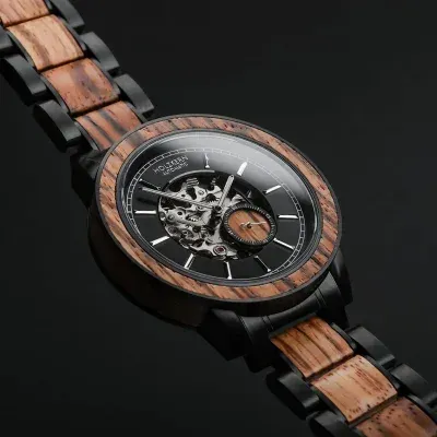 Nahaufnahme einer schwarzen Armbanduhr mit hölzerne Armband und Zifferblatt, das mechanisches Uhrwerk mit beweglichen Teilen zeigt.