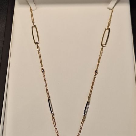 Eine goldene Halskette mit ovalen Gliedern und kleinen Diamantakzenten wird in einer weißen Schachtel präsentiert. Die Schachtel ist geöffnet und zeigt das elegante Design der Halskette.