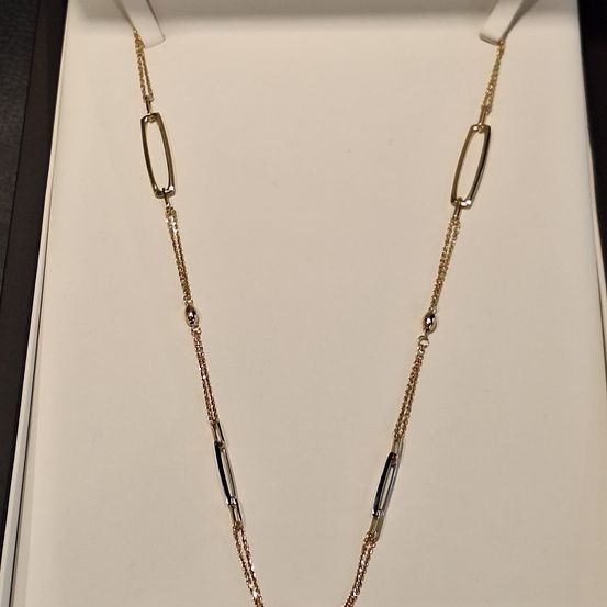 Eine goldene Halskette mit ovalen Gliedern und kleinen Diamantakzenten wird in einer weißen Schachtel präsentiert. Die Schachtel ist geöffnet und zeigt das elegante Design der Halskette.