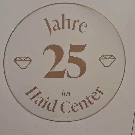 Ein rundes Schild mit goldenem Rand zeigt die Nummer 25 und die Worte 'Jahre 25 im Haid Center'. Zwei Diamantsymbole befinden sich auf beiden Seiten der Nummer.