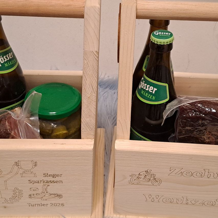 Zwei Holzkisten enthalten Bierflaschen und Gläser. Eine Kiste hat ein Glas mit Essiggurken, ein Fleischstück und ein Etikett mit 'Sieger Sparkassen Turnier 2026'. Die andere Kiste hat ein Glas mit Essiggurken, eine Bierflasche und ein Etikett mit 'Zechhaus Werkzeit'.